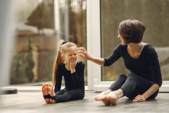 Laughing mother sitting with daughter on floor inside home.
