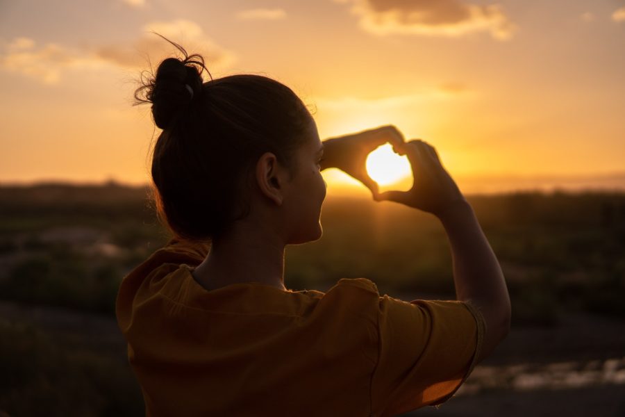Young woman making the shape of a heart with her hands over the sun.